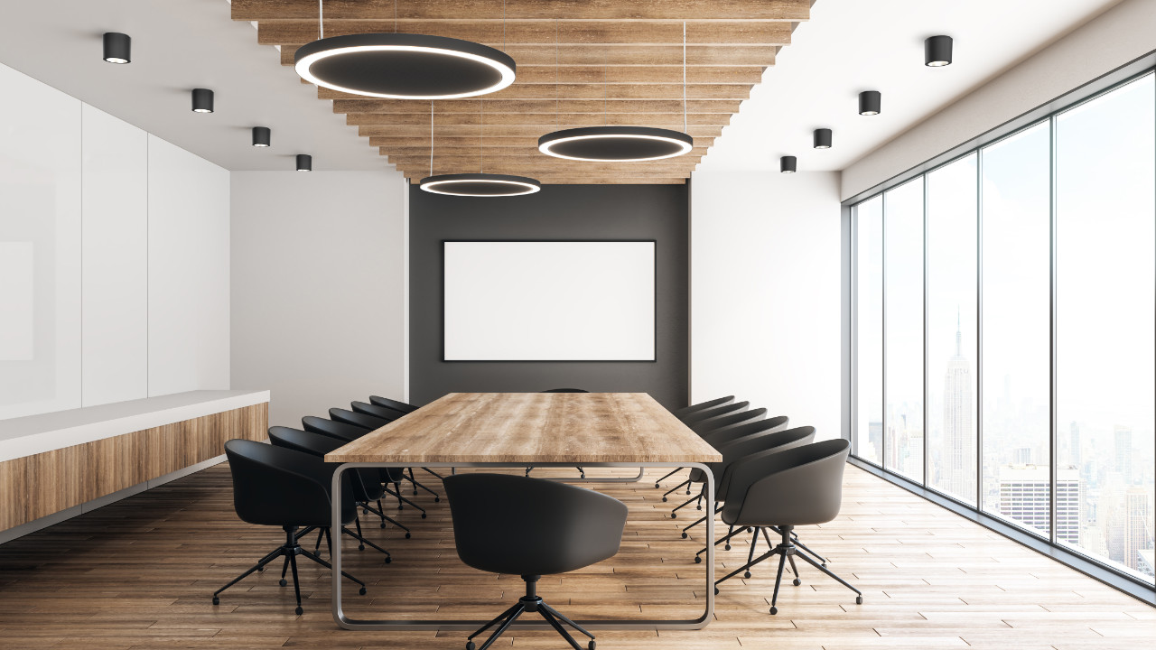 Moderner Konferenzraum mit langem Holztisch, schwarzen Stühlen und großen Fensterfronten.