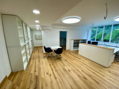 Büroraum mit rustikalem Holzboden, einem Besprechungstisch, Regal und Arbeitsplatz mit einem Aktenschrank