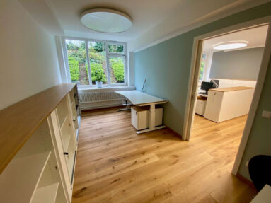 Kleines Büro mit rustikalem Holzboden, Regal, Schreibtisch und Durchgang in ein anderes Büro.