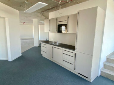 Büroküche mit weißen Fronten und schwarzer Arbeitsplatte.