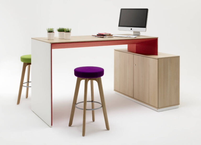 Steharbeitsplatz-Arrangement mit zwei Stehhockern, einem Tisch, der an ein Schrank-/Sideboardelement angebaut ist. Farbigkeit: Holz + Farbakzent rot